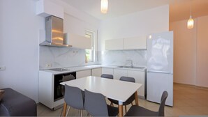 A modern kitchen with white cabinets, a stainless steel range hood, a built-in oven, a refrigerator, and a dining area with a table and chairs. - Lura Apartment 04 in Plazhi San Pietro (Plazhi San Pietro)