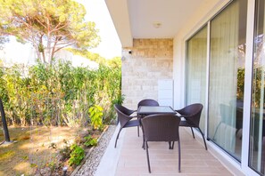 A patio with a table and chairs, a stone wall, and a glass door. - SanPietro Vacation Apartment 051 (Plazhi San Pietro)