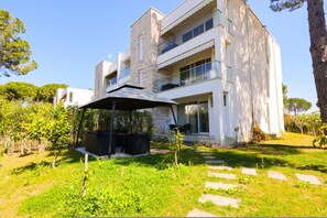 A modern two-story building with a stone facade, a covered outdoor seating area, and a well-maintained garden. - SanPietro Vacation Apartment 051 (Plazhi San Pietro)