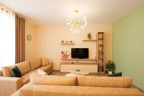 Ein Wohnzimmer mit einer Sofagarnitur, einem Fernseher, einem Couchtisch und einer dekorativen Lampe.