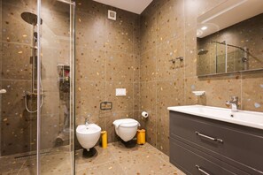 Ein modernes Badezimmer mit Duschkabine aus Glas, zwei Waschbecken, einer Toilette und einem Waschtisch mit Schubladen.