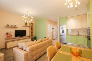 A modern living room with a sofa, TV, and dining area with chairs and a table. - SanPietro Vacation Apartment 055 (Plazhi San Pietro)
