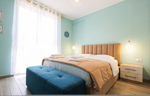 A bedroom with a bed, a bedside table, a clock, and a window with curtains. - SanPietro Vacation Apartment 055 (Plazhi San Pietro)