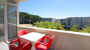En balkon med et bord og stole, udsigt til bygninger og træer.