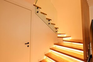 A staircase with wooden steps and a glass railing, leading to a door with a handle. - SanPietro Premium Villa 015 (Durrës)