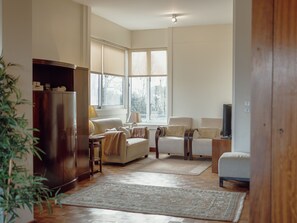 Ein Wohnzimmer mit einer Couch, Sesseln, einem Couchtisch, einem Fernseher und einem Bücherregal.