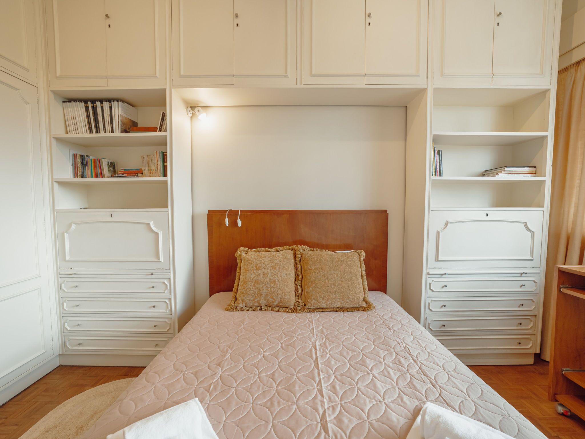 A bedroom with a large bed, two bedside tables, a wardrobe, and built-in shelving with books.