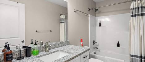 A modern bathroom with a granite countertop, a white sink, a mirror, a shower with a curtain, and a toilet.