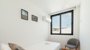 A small, single-bed room with a window, a chair, and two wall-mounted air conditioning units. - Apartment  by Interhome (Porto)