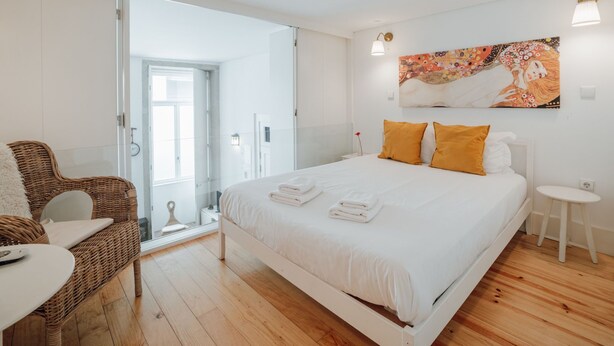 Un dormitorio moderno con una cama grande, una silla de mimbre y una mesita.