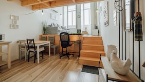 Un interior acogedor con una mesa de comedor de madera, sillas, una silla de oficina negra, una escalera y un gallo de cerámica blanca.