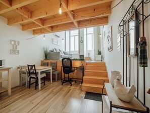 A cozy interior with a wooden dining table, chairs, a black office chair, a staircase, and a white ceramic rooster. - HISTORIC & BRIGHT BOLHAO MEZZANINE by VACATIONY by Interhome (Porto)