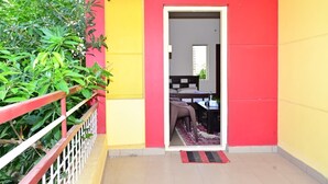 Une pièce comprenant un lit, un bureau et une chaise, avec un mur extérieur rouge et jaune et une plante verte à l’extérieur.