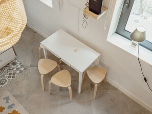 Une pièce avec une table blanche et deux chaises, une lampe suspendue et une fenêtre donnant sur un paysage.