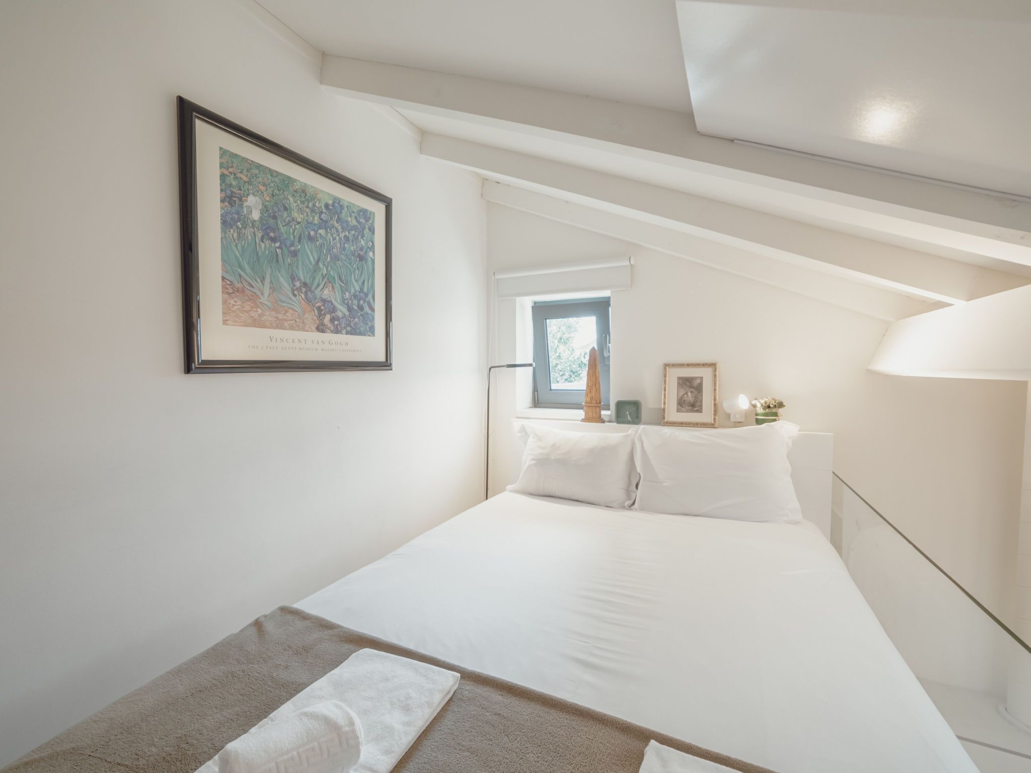 Een slaapkamer met een bed, een lijstwerk aan de muur, een raam en een nachtkastje met een lamp.
