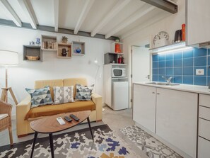 A compact living space with a sofa, a small coffee table, a kitchenette with a microwave, and a sink. - Apartment  by Interhome (Porto)