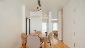 A modern dining area with a wooden table and chairs, an air conditioning unit above, and a view into a bedroom with a bed and curtains. - Apartment  by Interhome (Porto)