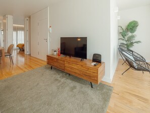 Un salon moderne avec un meuble TV en bois, un téléviseur à écran plat, une télécommande et un haut-parleur NOOS.