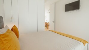 A bedroom with a bed, a television, and a door leading to another room. - Apartment  by Interhome (Porto)