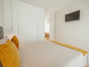 Um quarto com uma cama, uma televisão e uma porta que dá para outro cômodo.