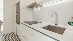 A modern kitchen with white cabinetry, a stainless steel sink, and a built-in range hood. - Apartment  by Interhome (Porto)