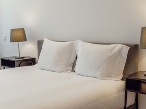 A neatly made bed with white linens, two bedside tables with lamps, and a plain wall. - Apartment  by Interhome (Porto)