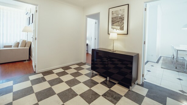 Ein geräumiger Wohnbereich mit kariertem Boden, einer Couch, einem Konsolentisch und einem gerahmten Bild an der Wand.