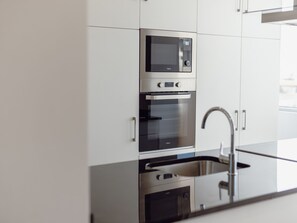 Une cuisine moderne équipée d’appareils électroménagers en acier inoxydable, notamment un four à micro-ondes, un four et un évier.