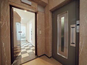 A hallway with a checkered floor, a door with a nameplate, and a wall-mounted elevator control panel. - Apartment  by Interhome (Porto)