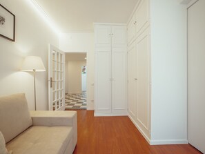 Un couloir avec un sol à carreaux, un canapé blanc, une lampe sur pied et une armoire.