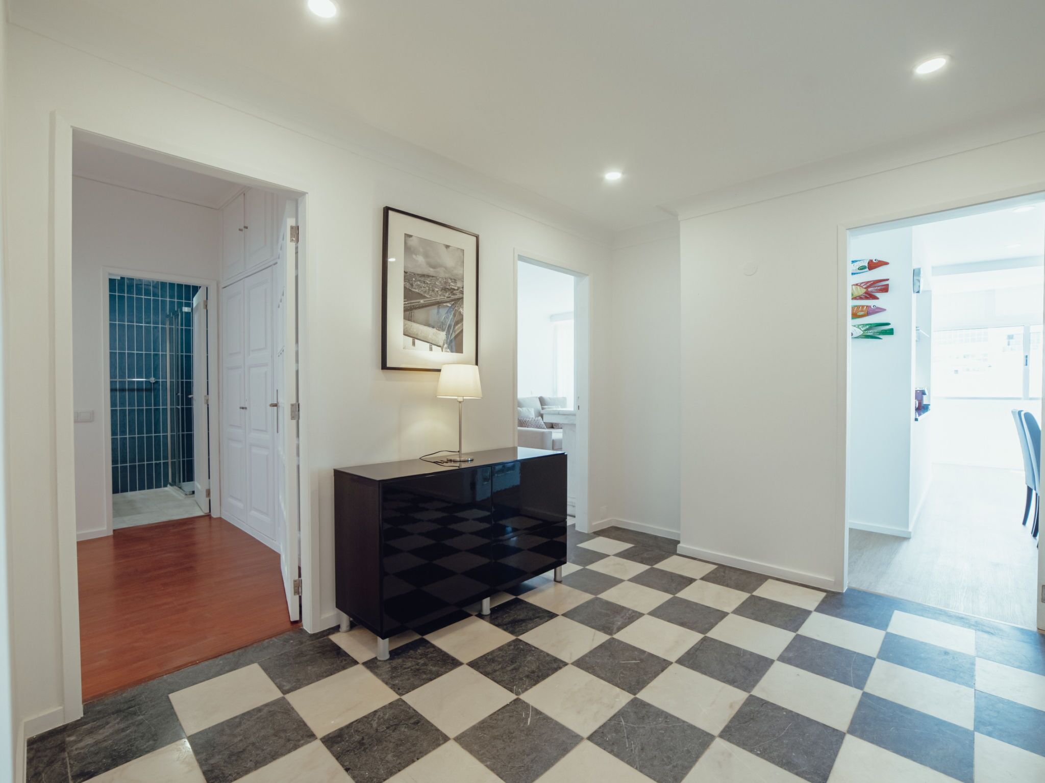 A hallway with a checkered floor, a black console table with a lamp, and a framed picture on the wall.