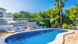 A swimming pool with lounge chairs and umbrellas, surrounded by greenery and a white fence. - Villa Talia by Interhome (Moraira)