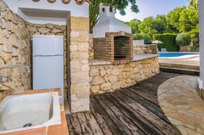 A stone-built outdoor kitchen with a built-in grill, a white refrigerator, and a poolside area. - Villa Talia by Interhome (Moraira)