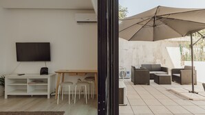 Ein modernes Wohnzimmer mit Flachbildfernseher, einem Holzesstisch und einer Sitzecke mit Gartenmöbeln.