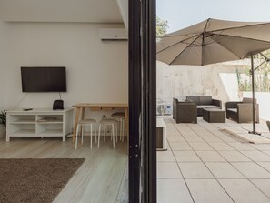Ein modernes Wohnzimmer mit Flachbildfernseher, einem Holzesstisch und einer Sitzecke mit Gartenmöbeln.
