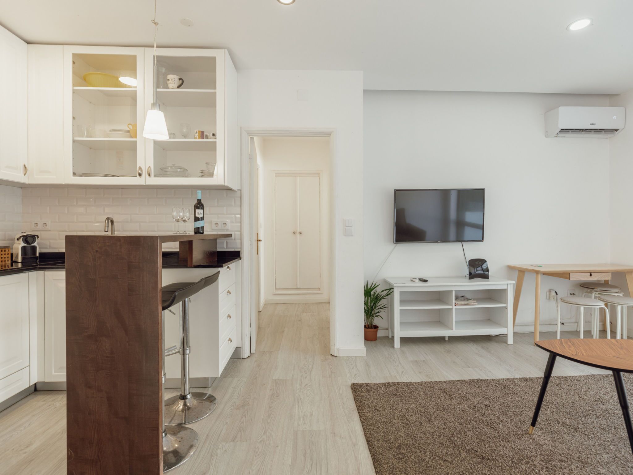 A modern kitchen with white cabinets, a dining area with a TV, and a wooden table.