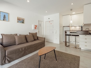 Een moderne woonkamer met een bank, een salontafel, en een keuken met kasten en een barkruk.