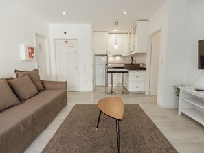 Ein modernes Wohnzimmer mit einem braunen Sofa, einem Holztisch und einer Küchenzeile mit weißen Schränken und einem Edelstahlkühlschrank.