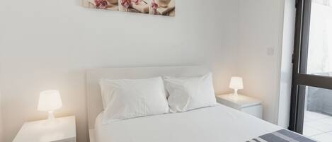 Une chambre d’hôtel comprenant un lit, deux tables de chevet avec des lampes, une fenêtre et un appareil de climatisation.