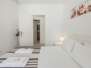 Een hotelkamer met een bed, nachtkastje, lamp en een deur naar een badkamer.