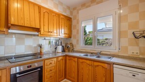 Una cocina con armarios de madera, horno empotrado, lavavajillas y ventana con vista a follaje.