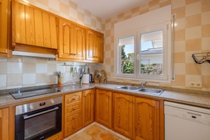 A kitchen with wooden cabinets, a built-in oven, a dishwasher, and a window with a view of greenery.