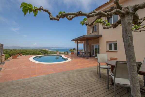 Zona de piscina con vistas al mar, mobiliario exterior y un edificio con patio empedrado.