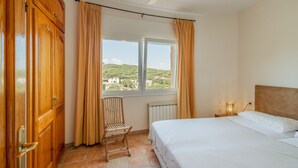 Un dormitorio con cama, una silla, una ventana con cortinas, un radiador y un ventilador de techo.