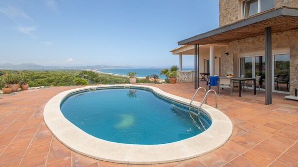 Una piscina con vistas al mar, un patio con mobiliario exterior y un edificio de piedra.