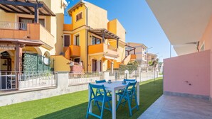 A patio with a table and chairs, a green lawn, and a building with balconies and a pink wall. - Affittimoderni Castelsardo - Our Villa (Castelsardo)