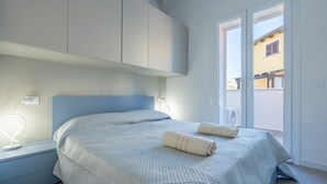 A bedroom with a bed, nightstand, and a window with a view of buildings. - Affittimoderni Castelsardo - Our Villa (Castelsardo)