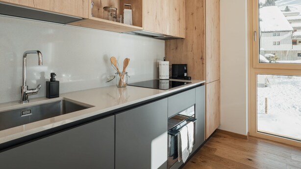 Une cuisine moderne avec des meubles en bois, un évier en acier inoxydable et une fenêtre donnant sur un paysage enneigé.