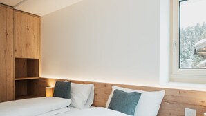 Une chambre à coucher avec une tête de lit en bois, un lit avec une literie blanche, une table de chevet et une fenêtre donnant sur des arbres.