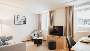 Un salon moderne comprenant un canapé, une petite table ronde, un téléviseur posé sur un meuble en bois, une chaise et une table à manger avec une assiette.